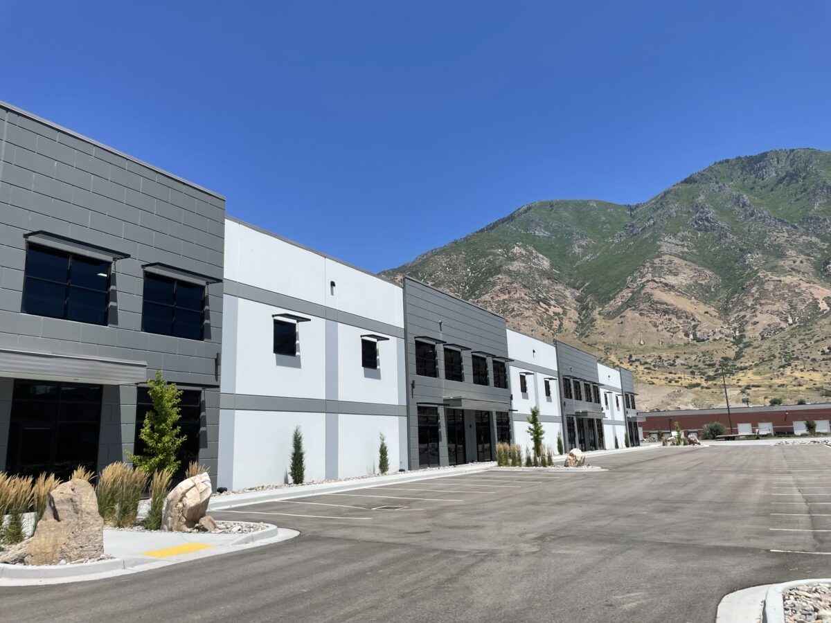 Modern commercial building with parking lot and mountains in the background.