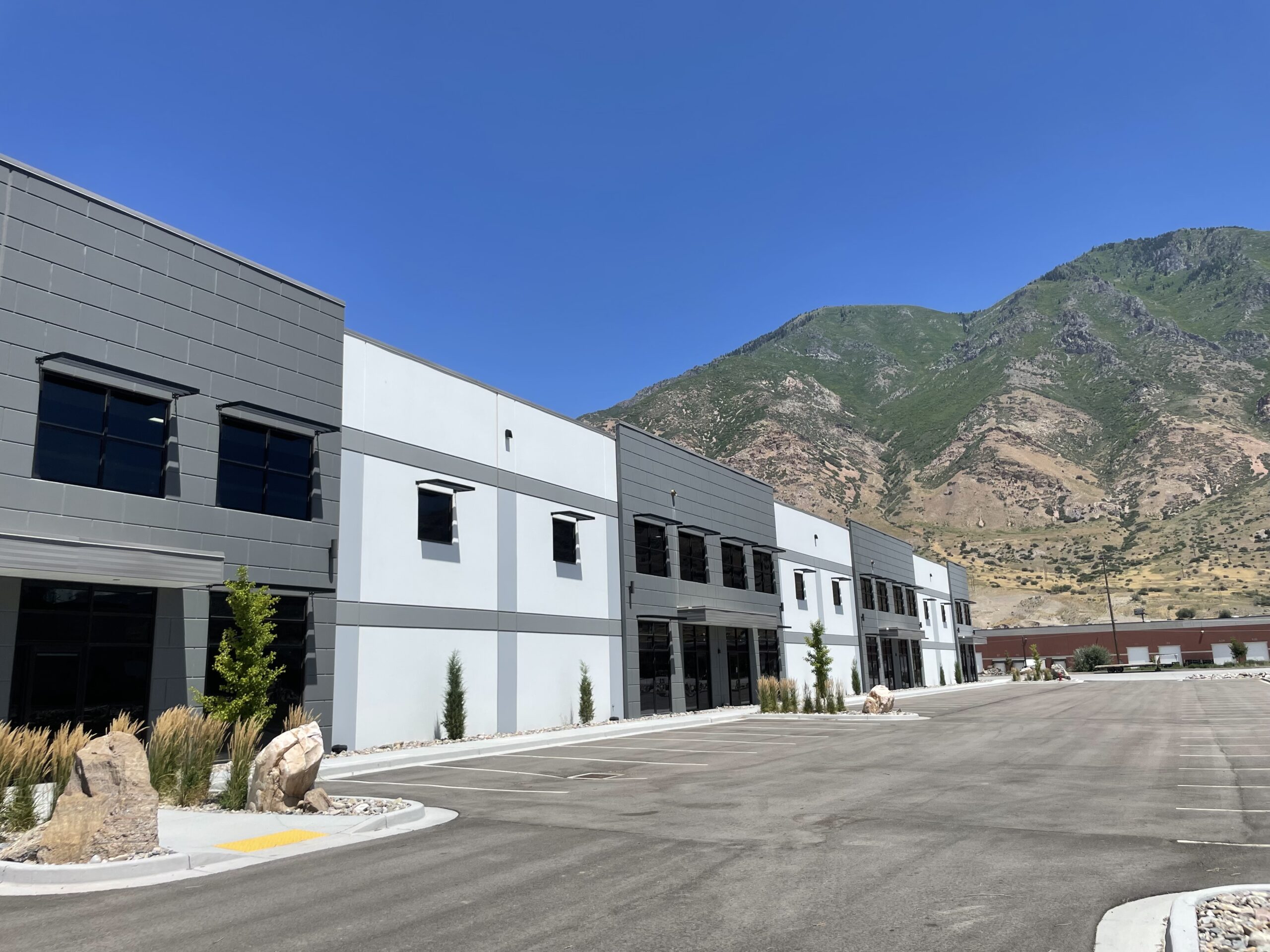 Modern commercial building with parking lot and mountains in the background.
